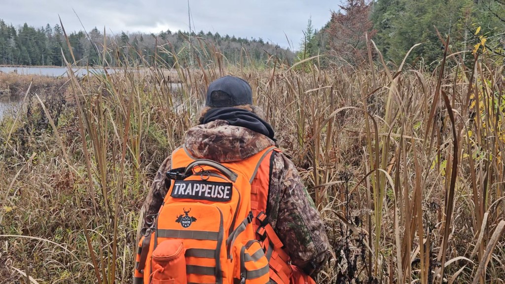Femme trappeuse en forêt au Québec avec sac à dos orange Trappeuse de Traktiq.